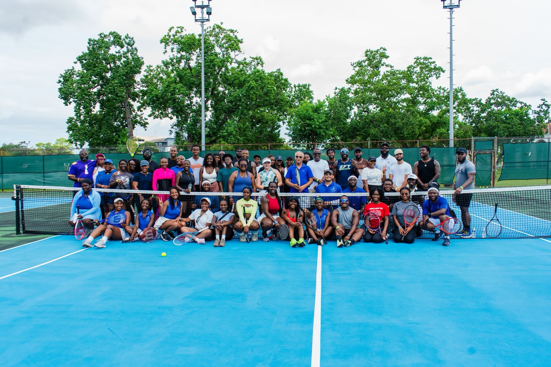 Elite Aces community group photo on a blue outdoor tennis court.